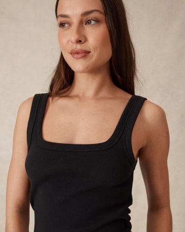 Woman wearing a black tank top against a beige background